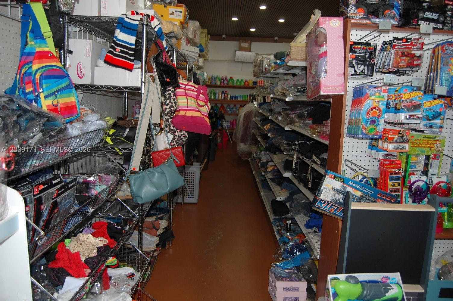 A narrow retail aisle features metal shelving units stocked with various toys, clothing, and accessories — 1900 e 4th ave, Hialeah FL 33010, HIALEAH, FL