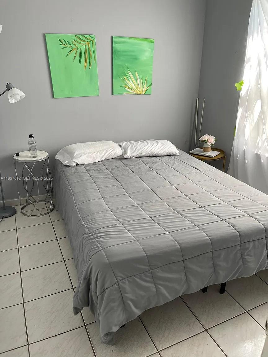 A bedroom features a bed with a gray comforter, two green paintings, and tile flooring — 638 SW 15th Ave, Miami FL 33135, MIAMI, FL