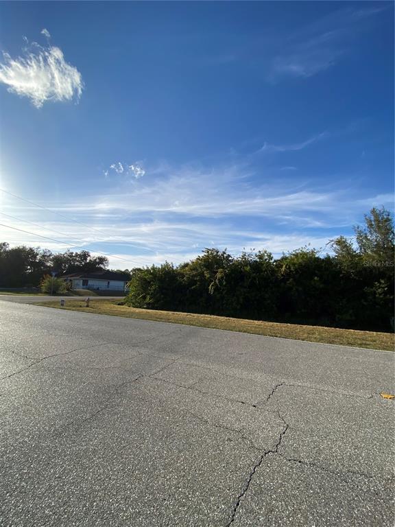 A paved road leads to a vacant, overgrown lot under a bright blue sky — Lot 19 EMBASSY ROAD, NORTH PORT, FL