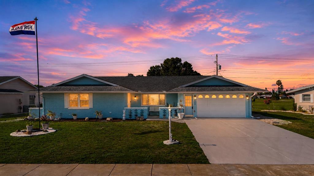 A light blue single-story house with a white garage door stands under a sunset sky — 624 LA JOLLA AVENUE, SUN CITY CENTER, FL