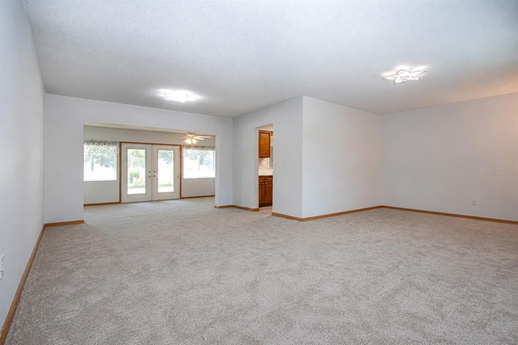 A spacious, carpeted living room features white walls, two ceiling lights, and a kitchen doorway — 624 LA JOLLA AVENUE, SUN CITY CENTER, FL