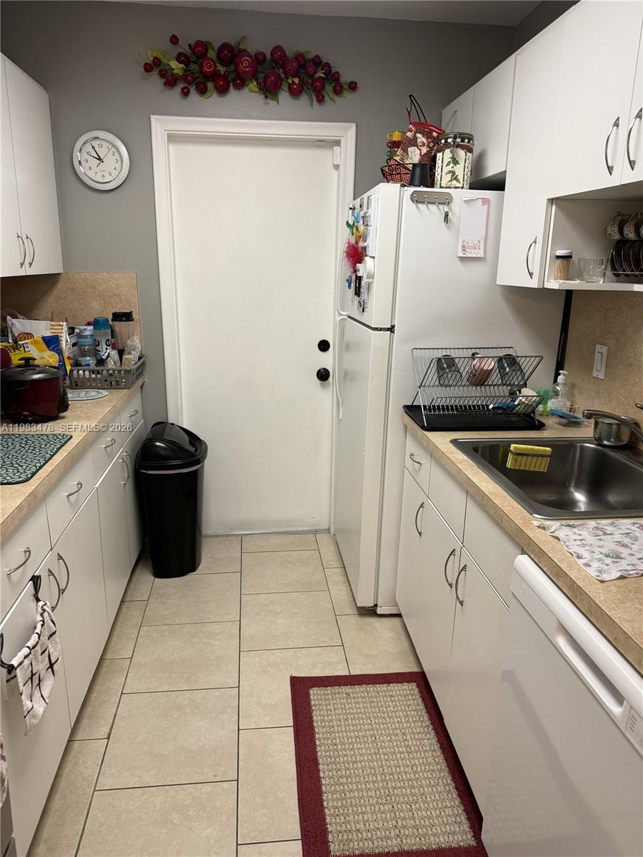 A galley kitchen features white cabinets, light countertops, a stainless steel sink, and tile flooring — 7845 Miller Dr # A204, Miami FL 33155, MIAMI, FL
