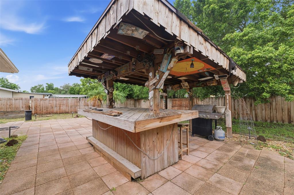 A wooden tiki bar with a covered roof sits on a paved patio in a backyard — 11105 ARECA DRIVE, PORT RICHEY, FL