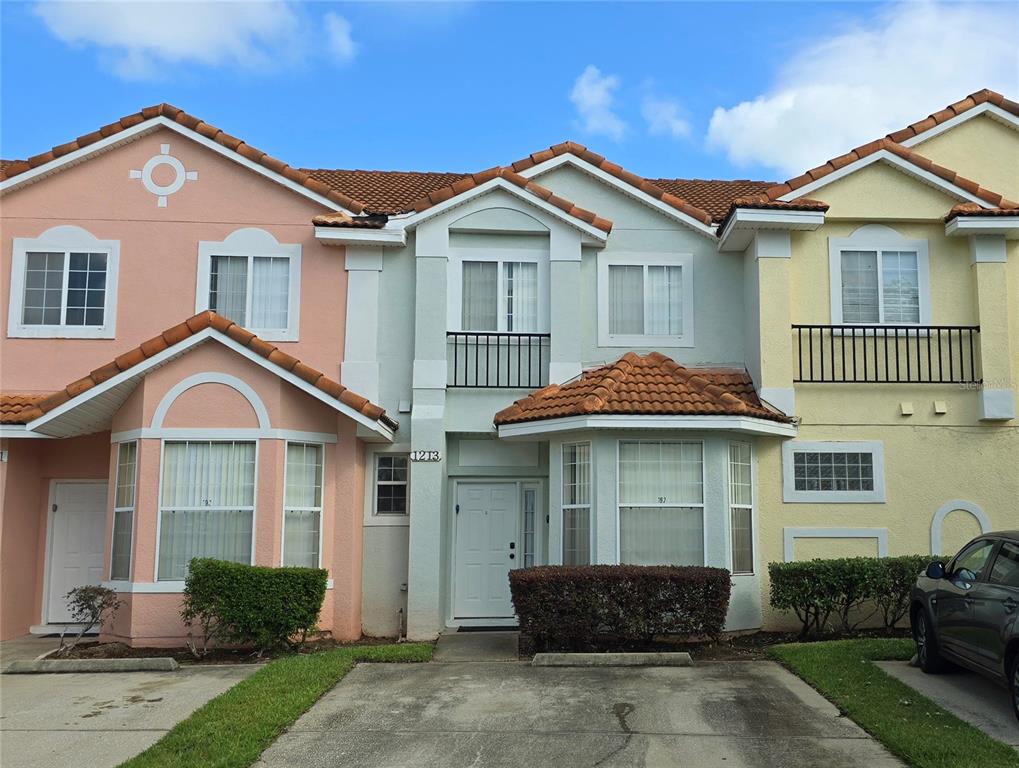A row of three attached townhomes with pastel-colored stucco facades and terracotta tile roofs — 1213 SOUTH BEACH CIRCLE, KISSIMMEE, FL