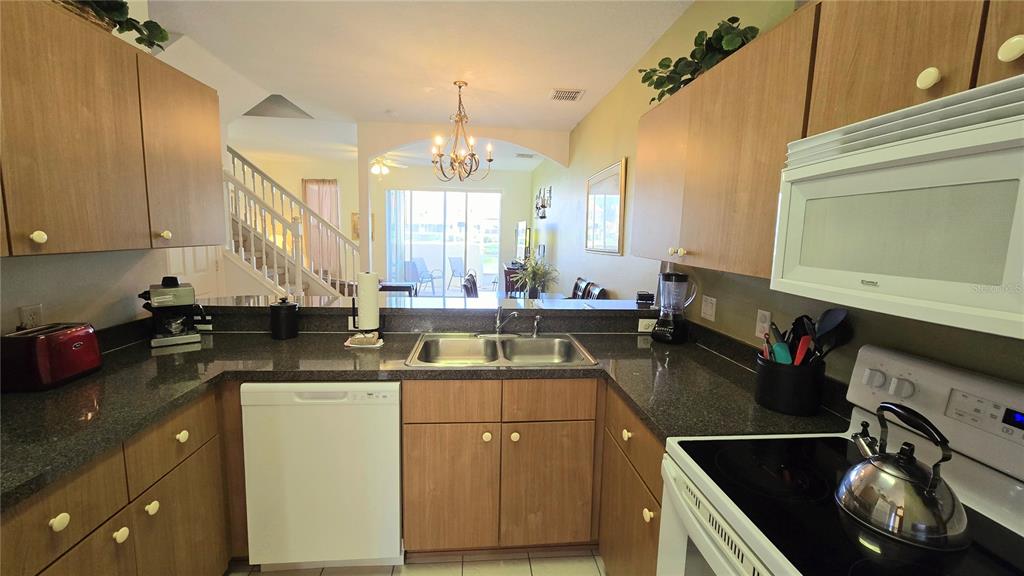 A kitchen with dark countertops and light wood cabinets overlooks a dining area — 1213 SOUTH BEACH CIRCLE, KISSIMMEE, FL