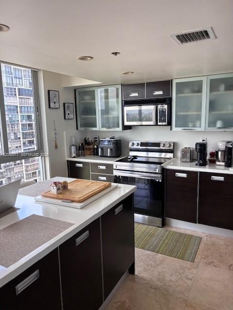 A modern kitchen features dark wood cabinetry, white countertops, stainless steel appliances, and large windows — 2025 Brickell Ave # 1903, Miami FL 33129, MIAMI, FL