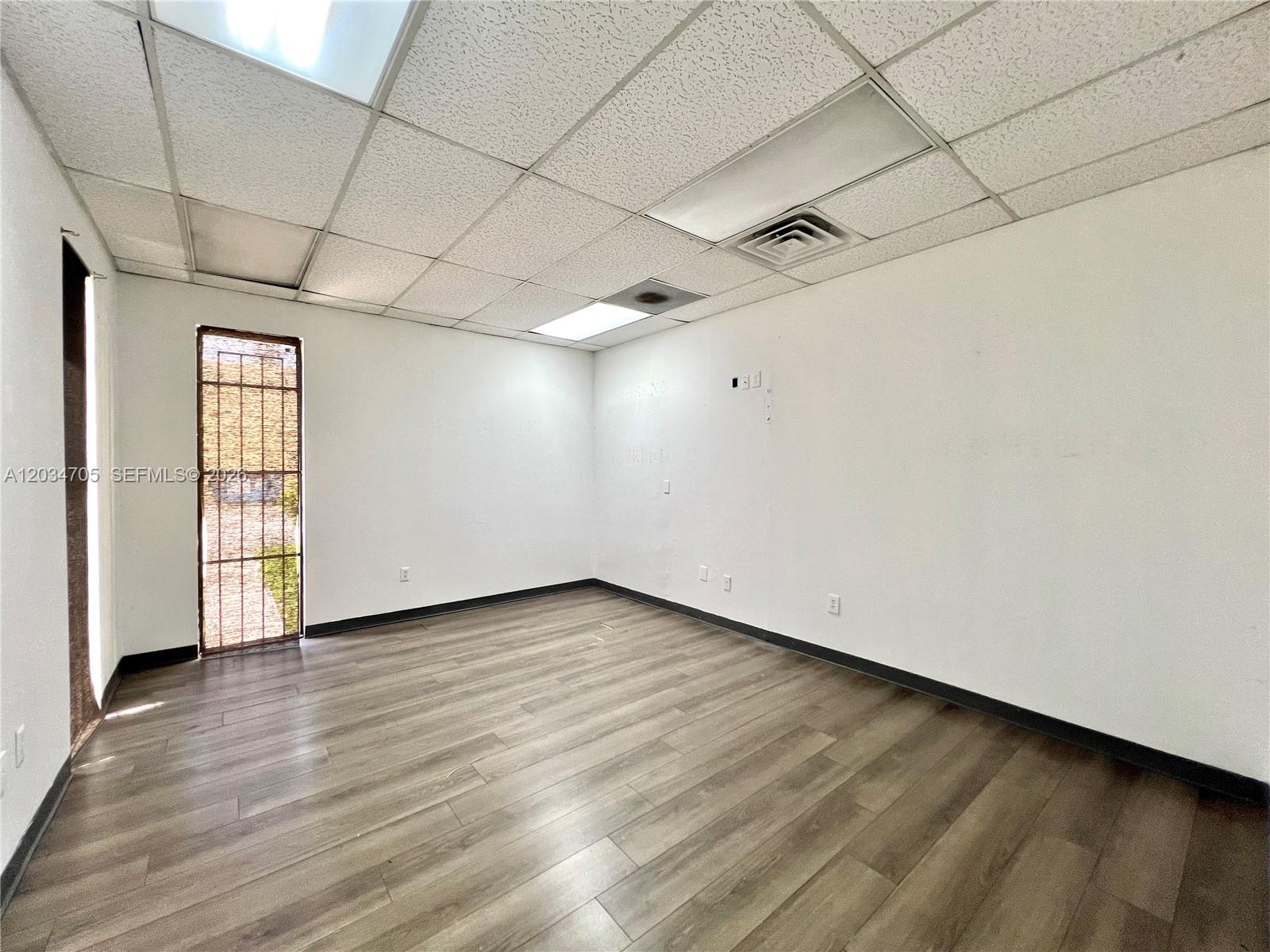 An empty office space features white walls, wood-look flooring, a drop ceiling, and a barred door — 3425 NW 73rd Ave, Miami FL 33122, MIAMI, FL