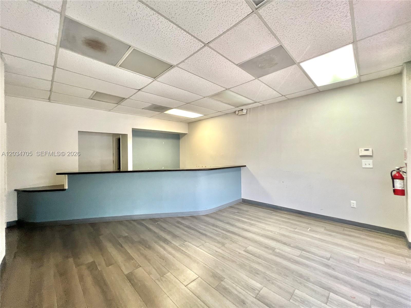 An empty commercial office space features a blue reception counter, drop ceiling, and wood-look flooring — 3425 NW 73rd Ave, Miami FL 33122, MIAMI, FL