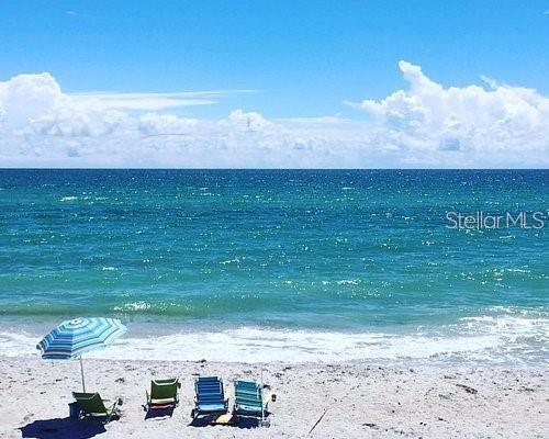 A blue and white striped beach umbrella stands over three chairs on a sandy beach — 2295 N BEACH ROAD UNIT 23, ENGLEWOOD, FL