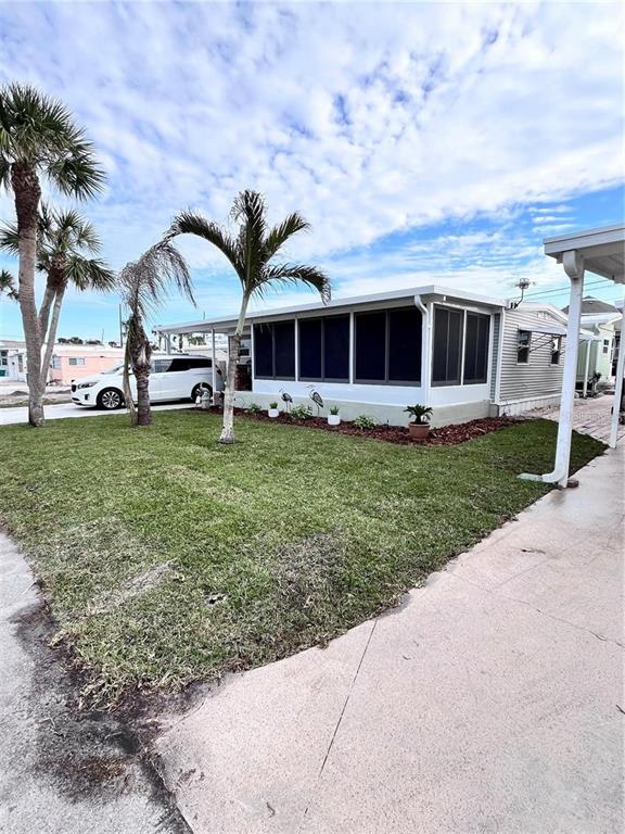 A light-colored mobile home features a screened-in porch, palm trees, and a grassy yard — 2295 N BEACH ROAD UNIT 23, ENGLEWOOD, FL