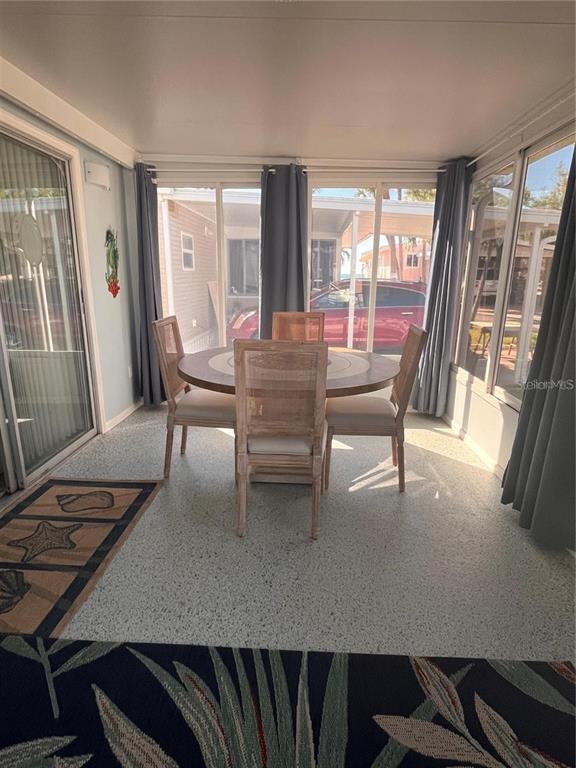 A sunroom features a round wooden dining table with four chairs and speckled flooring — 2295 N BEACH ROAD UNIT 23, ENGLEWOOD, FL