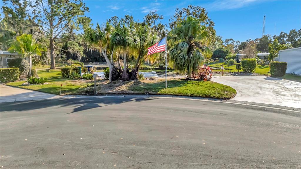 An American flag stands in a grassy yard between two driveways near a small pond — 722 LANDRY LANE, TAVARES, FL