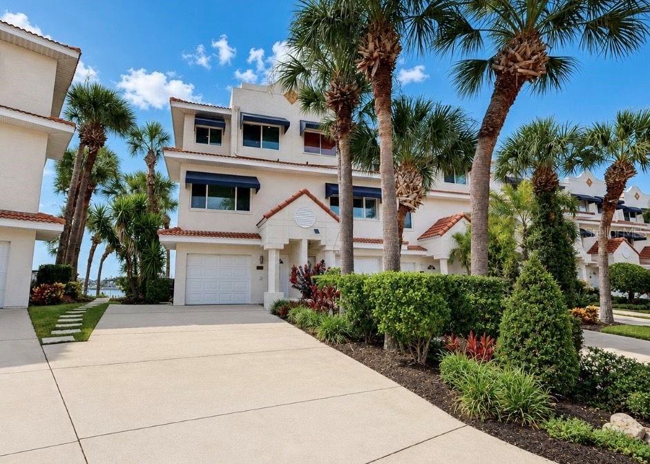 A three-story townhouse with a white stucco facade, a garage, and palm trees in front — 4639 MIRABELLA COURT, ST PETE BEACH, FL