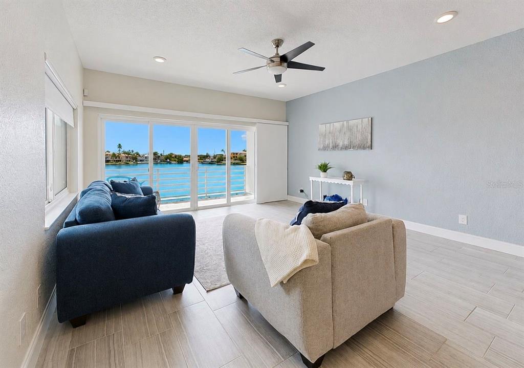 A living room features light tile floors, a blue sofa, and sliding glass doors overlooking water — 4639 MIRABELLA COURT, ST PETE BEACH, FL