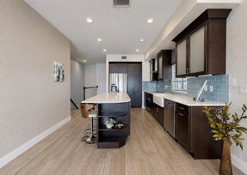 A modern kitchen features dark wood cabinets, a white island, and light blue subway tile — 4639 MIRABELLA COURT, ST PETE BEACH, FL
