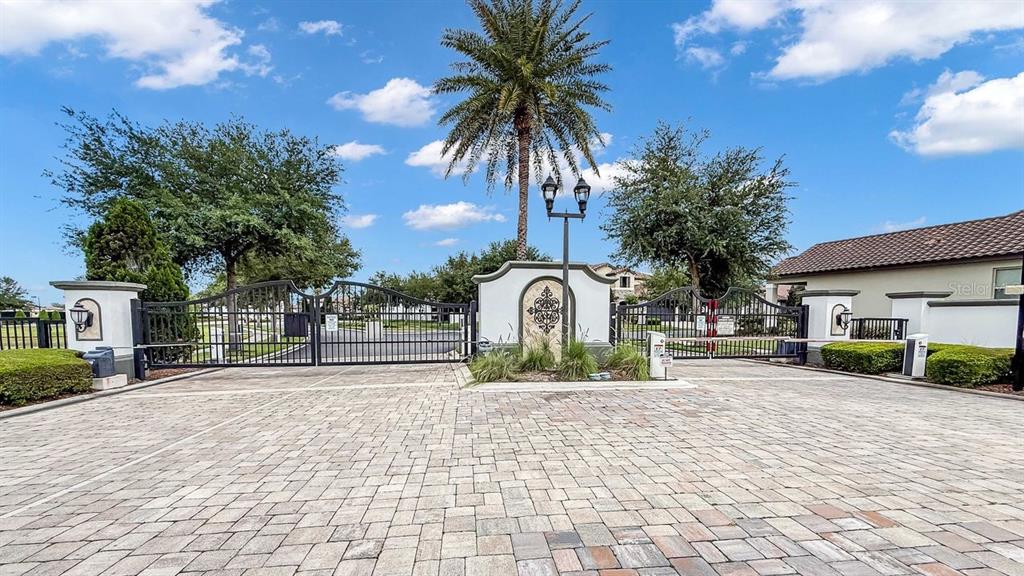 A paved driveway leads to a gated entrance with a palm tree and stone pillars — 10944 CITRON OAKS DRIVE, ORLANDO, FL