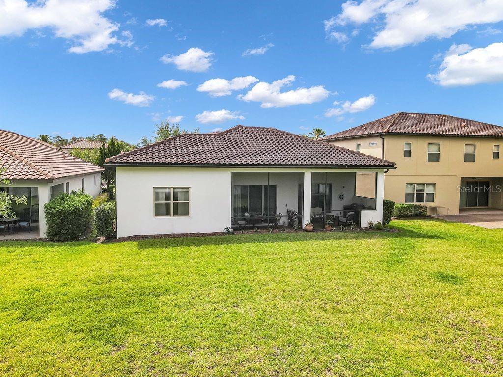 The backyard of a house features a screened-in patio and a large grassy lawn — 10944 CITRON OAKS DRIVE, ORLANDO, FL