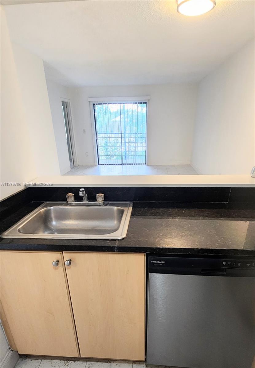A kitchen sink and dishwasher are set against a black countertop facing a living area — 902 NE 209 St # 40, Miami FL 33179, MIAMI, FL