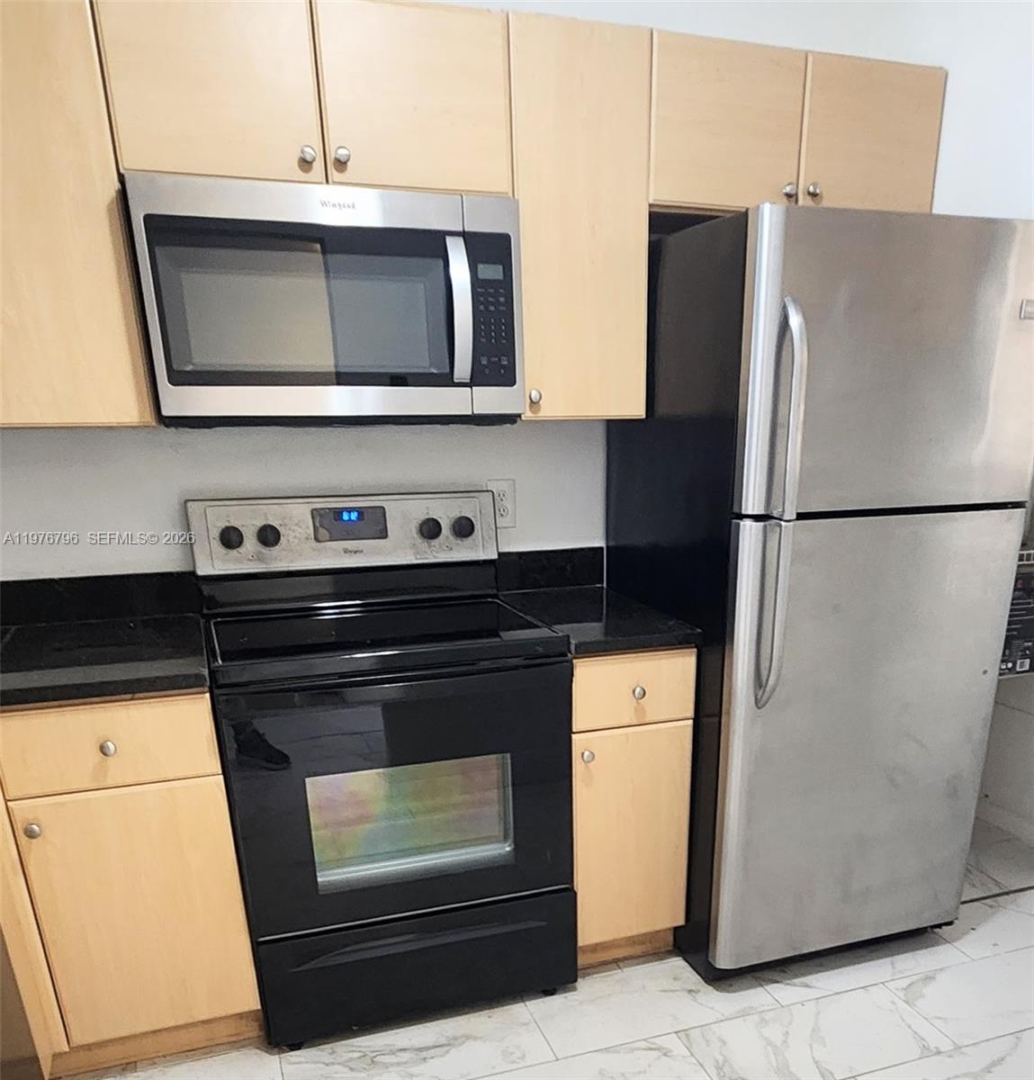 A kitchen features light wood cabinets, black countertops, and stainless steel appliances — 902 NE 209 St # 40, Miami FL 33179, MIAMI, FL