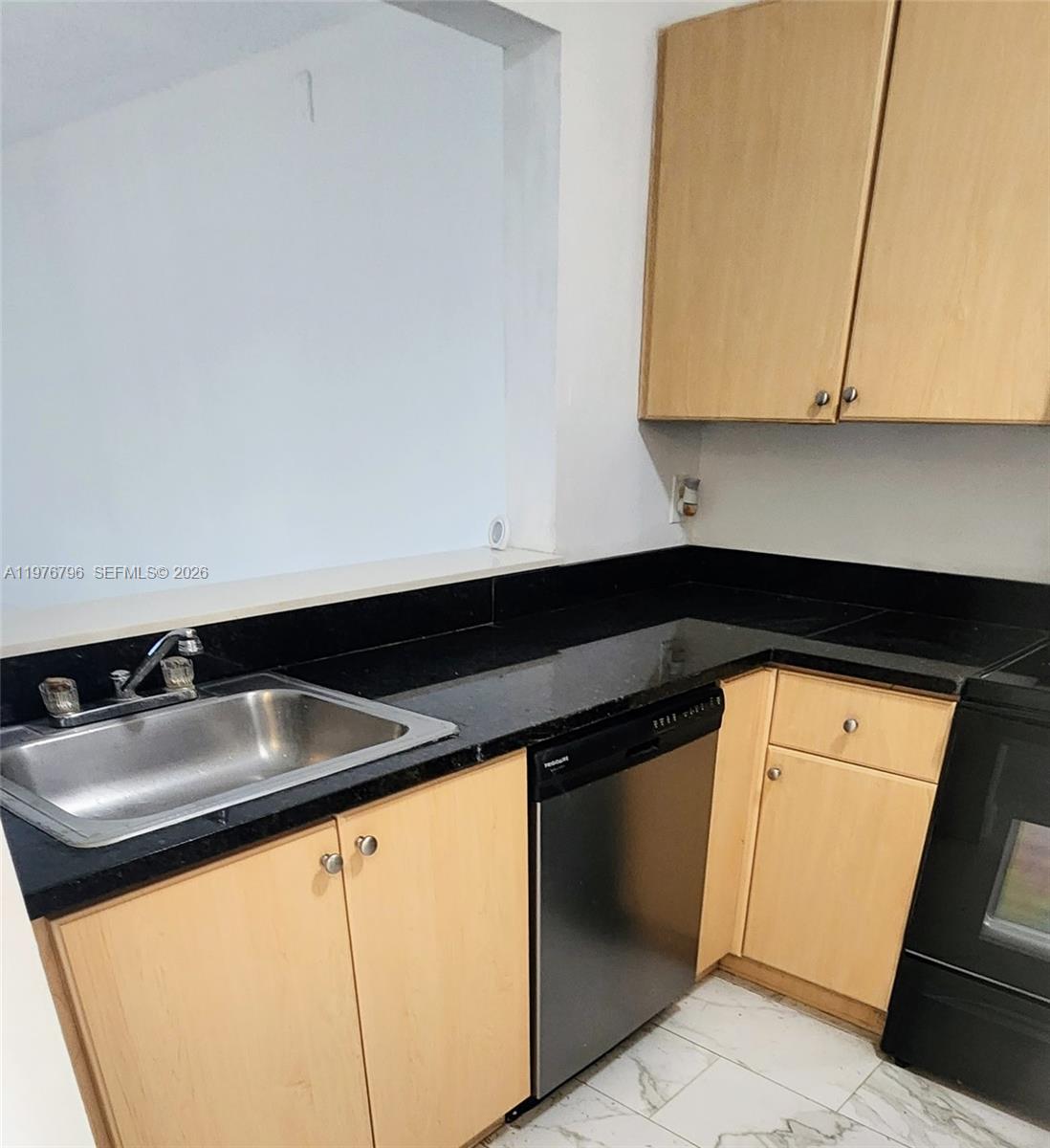 A kitchen features light wood cabinets, black countertops, a stainless steel sink, and black appliances — 902 NE 209 St # 40, Miami FL 33179, MIAMI, FL