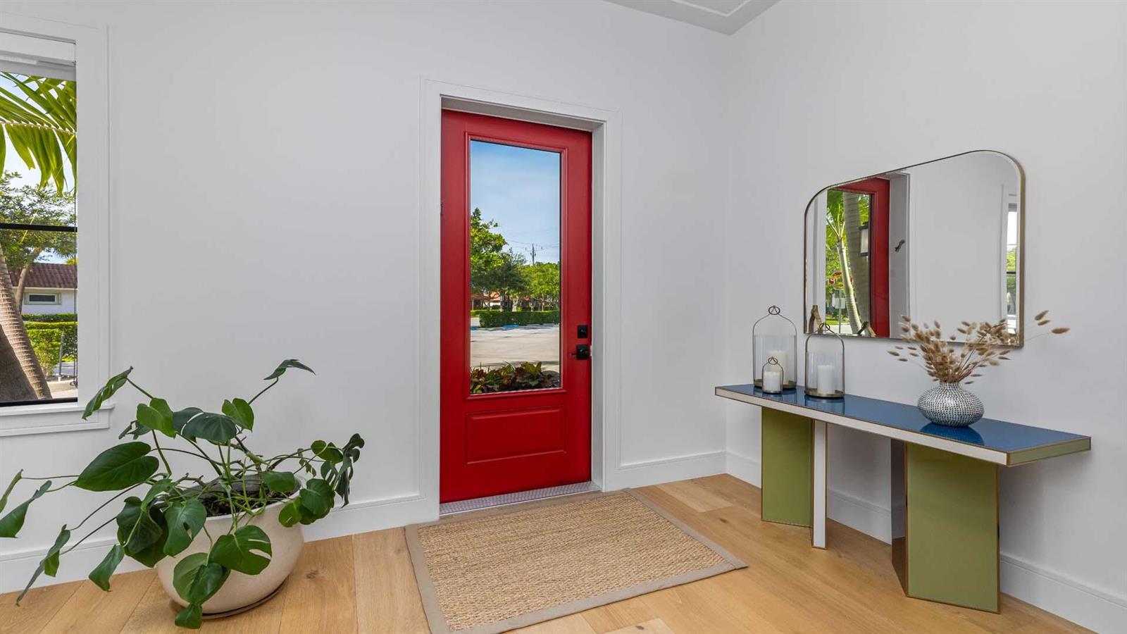 An entryway features light wood floors, a red front door, and a modern console table — 230 George Bush Boulevard, Delray Beach FL 33444, DELRAY BEACH, FL