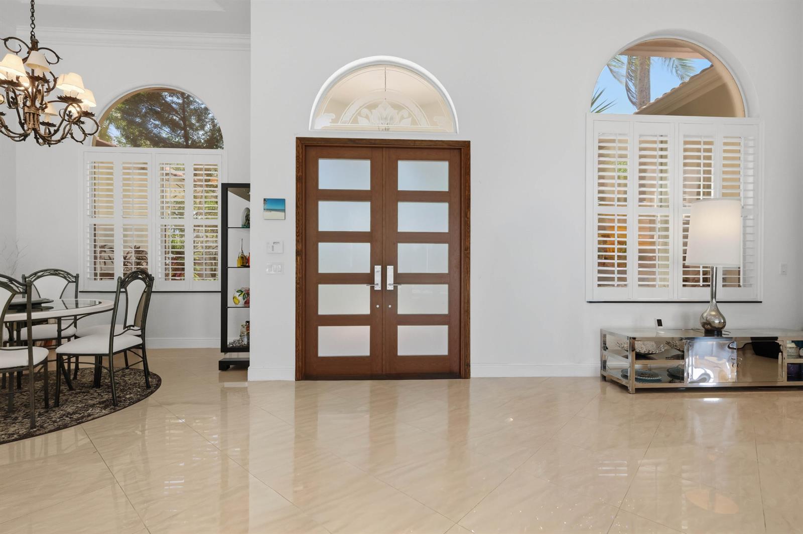 A bright foyer features a double wooden door, arched windows, plantation shutters, and polished tile floors — 7079 NW 68th Drive, Parkland FL 33067, PARKLAND, FL