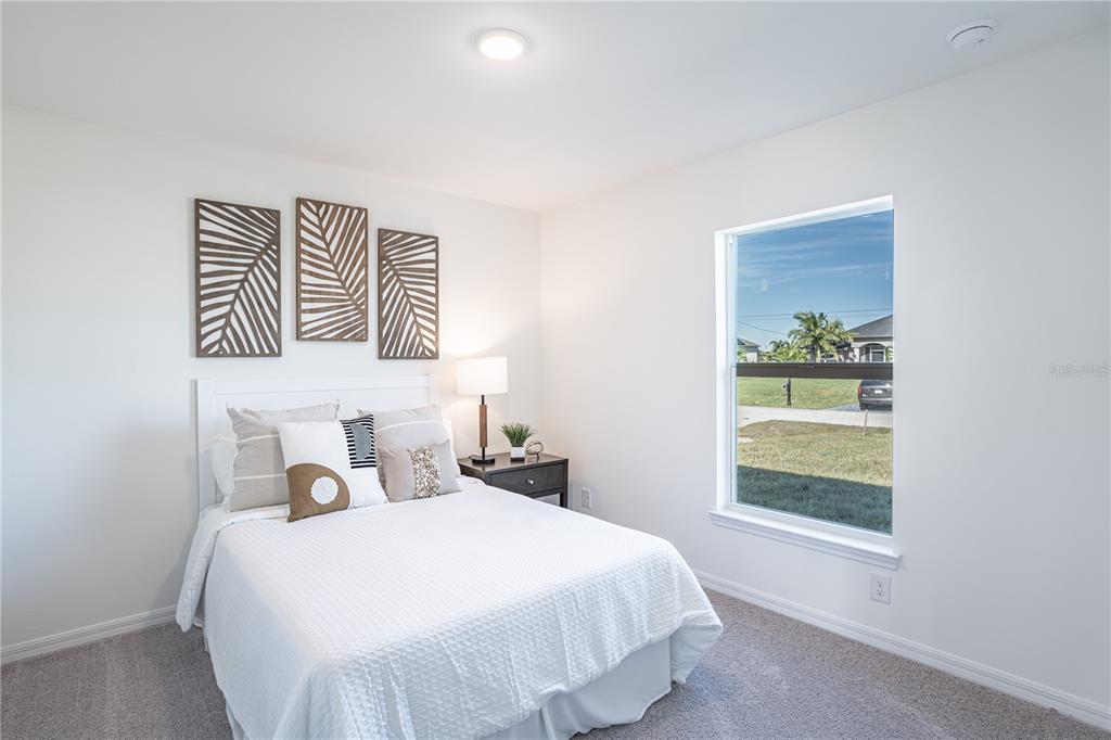A bedroom features a white bed, three wall art panels, and a window with views — 2107 KADER STREET, PORT CHARLOTTE, FL