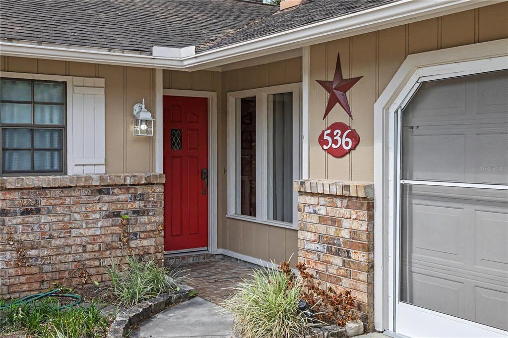A brick and tan siding house exterior features a red front door and address plaque — 536 NE 40TH AVENUE, OCALA, FL