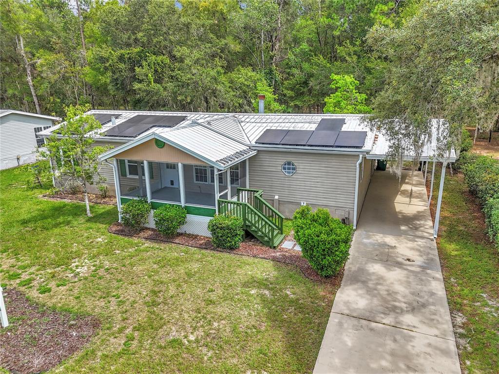 An exterior view of a single-story home with a metal roof, solar panels, and carport — 7899 W FOSTORIA DRIVE, DUNNELLON, FL