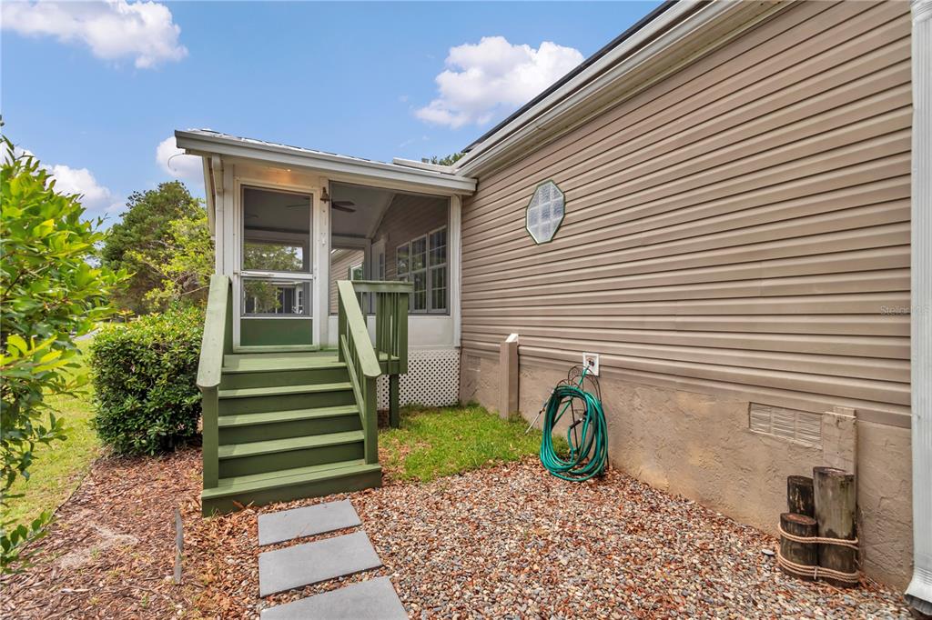 A green wooden staircase leads to a screened-in porch on the side of a house — 7899 W FOSTORIA DRIVE, DUNNELLON, FL