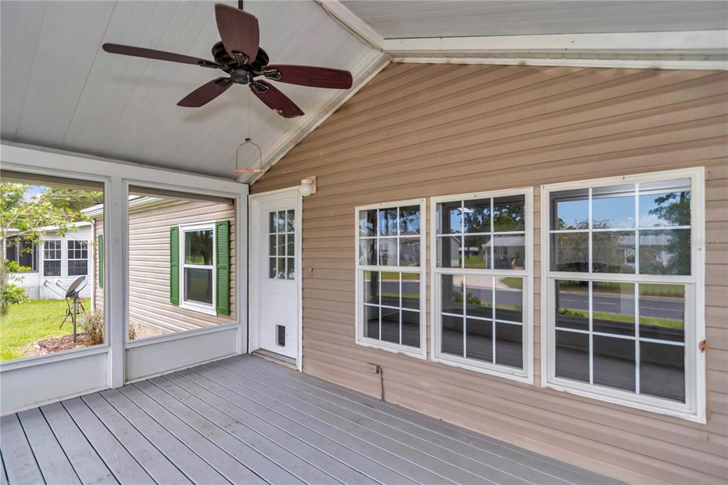 A covered porch features gray wooden decking, a ceiling fan, and tan vinyl siding — 7899 W FOSTORIA DRIVE, DUNNELLON, FL