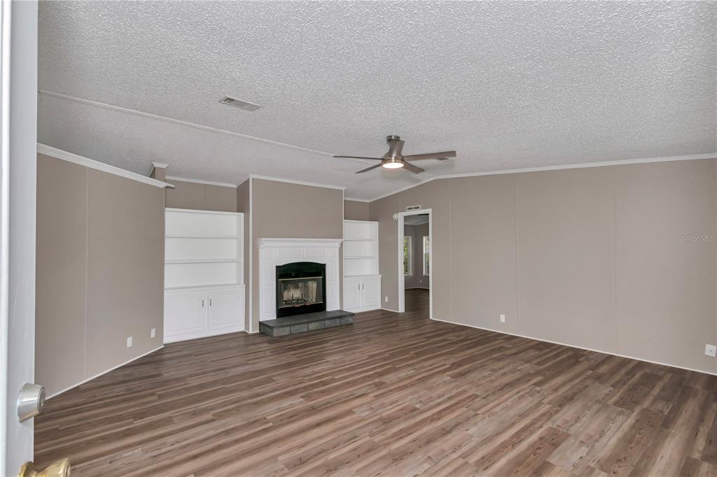 A living room features wood-look flooring, a fireplace with built-in shelving, and a ceiling fan — 7899 W FOSTORIA DRIVE, DUNNELLON, FL