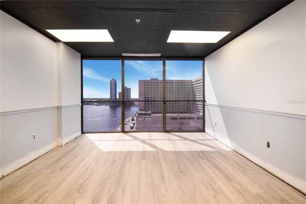 An empty room with light wood flooring, a black drop ceiling, and floor-to-ceiling waterfront windows — 233 E BAY STREET UNIT 1101, JACKSONVILLE, FL