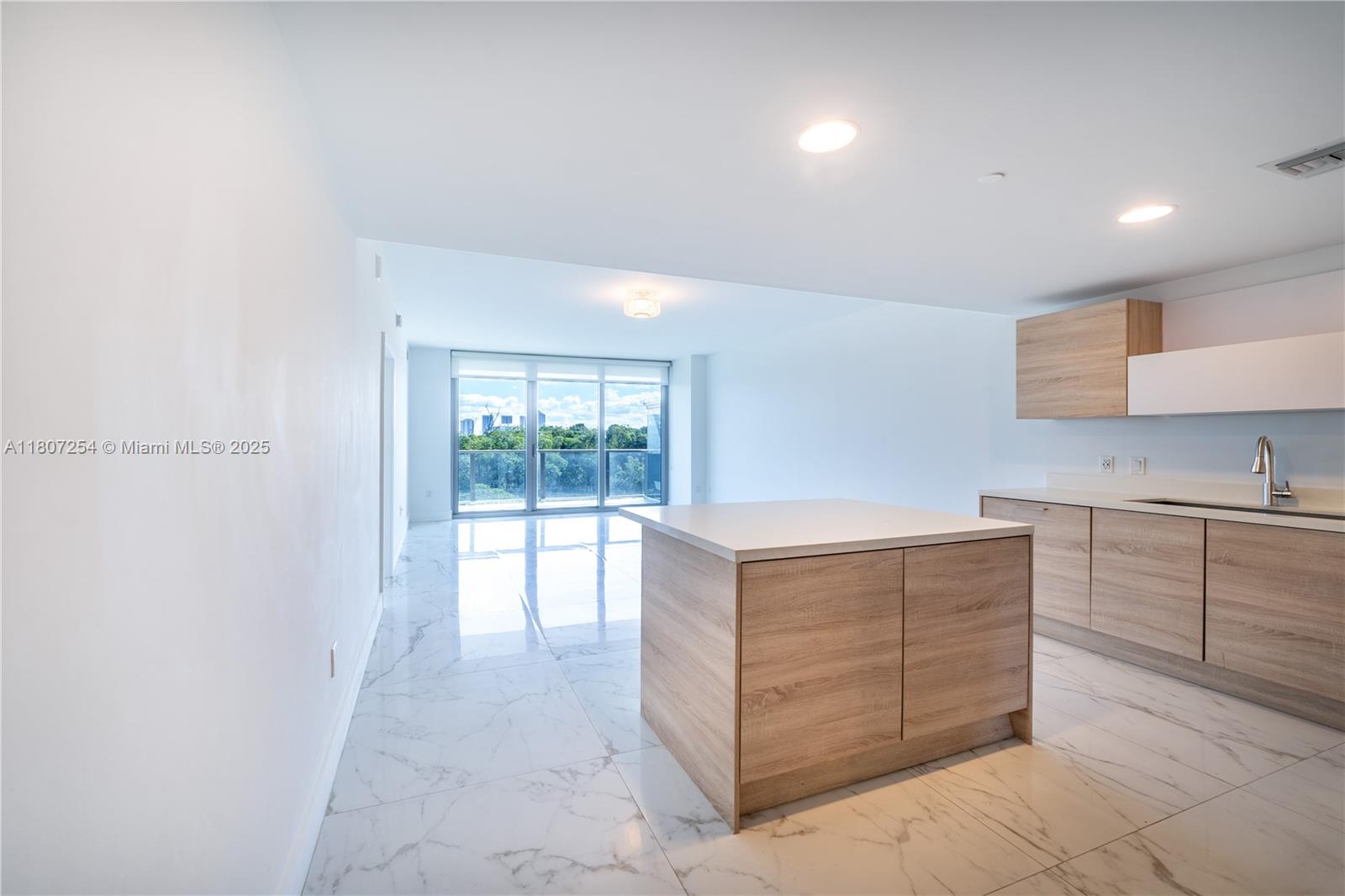 A modern kitchen features light wood cabinetry, a central island, and white marble-patterned tile flooring — 16385 Biscayne Blvd # 417, North Miami Beach FL 33160, NORTH MIAMI BEACH, FL
