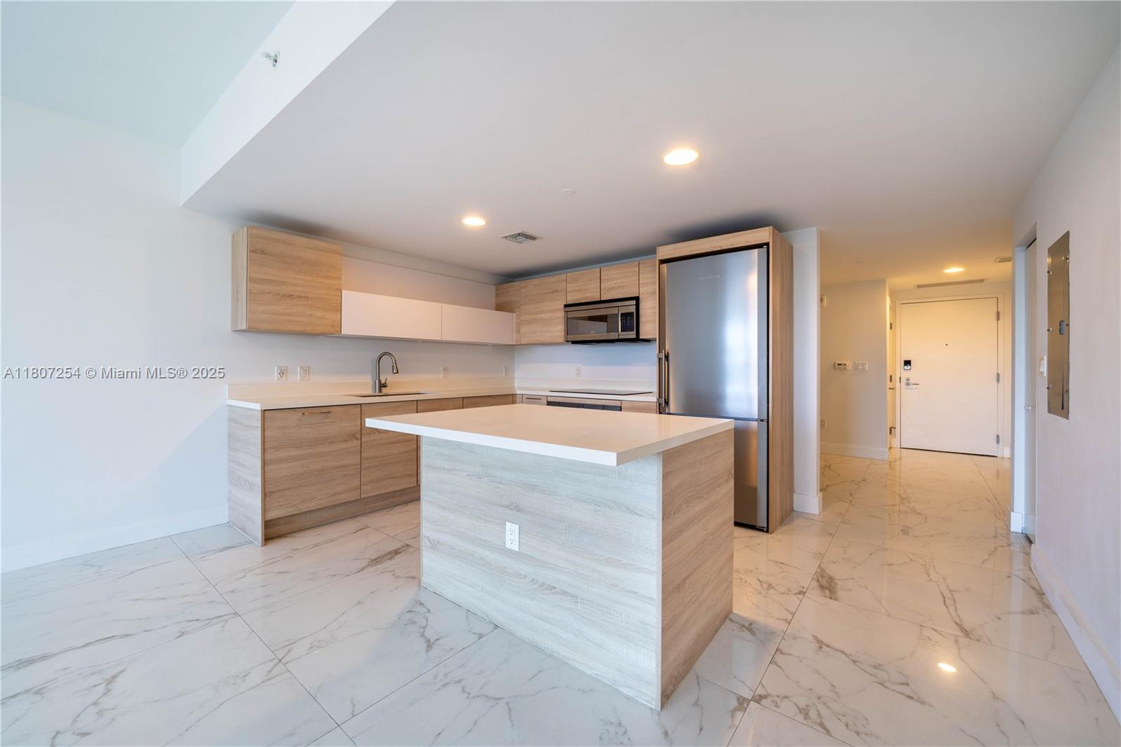 A modern kitchen features light wood cabinets, white countertops, and white marble-patterned tile flooring — 16385 Biscayne Blvd # 417, North Miami Beach FL 33160, NORTH MIAMI BEACH, FL