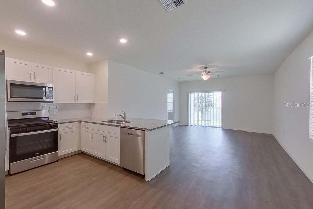 A kitchen with white cabinets and stainless steel appliances opens into a spacious living area — 31942 KATELIN CIRCLE, LEESBURG, FL
