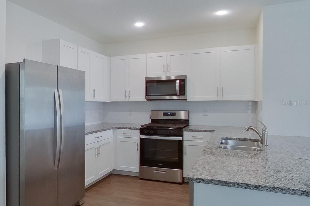 A modern kitchen features white cabinets, stainless steel appliances, and granite countertops — 31942 KATELIN CIRCLE, LEESBURG, FL