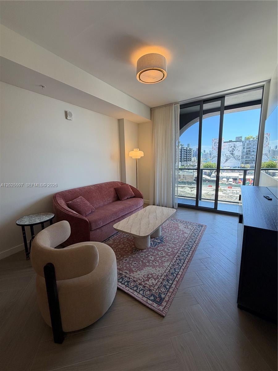 A living room features a pink sofa, a cream armchair, and a balcony with city views — 2700 NW 2nd ave # 416, Miami FL 33127, MIAMI, FL