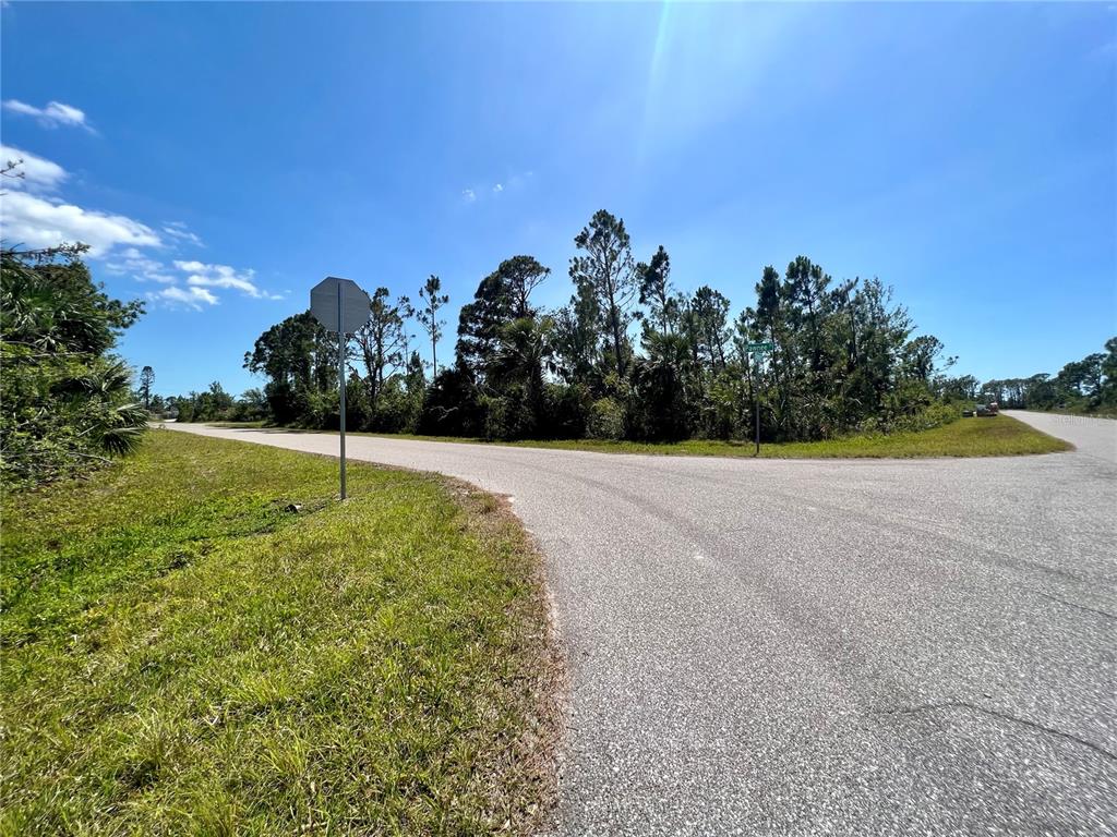 A paved road intersection features a stop sign and dense trees under a blue sky — 12143 STORKE AVENUE, PORT CHARLOTTE, FL