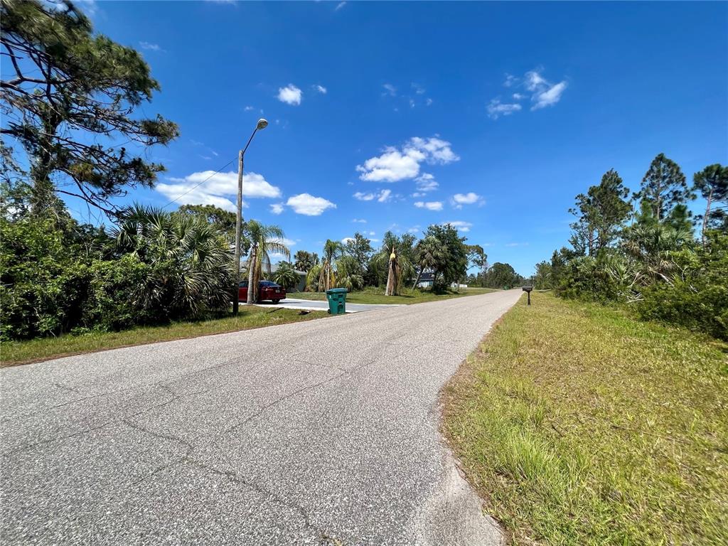 A paved residential street lined with trees, a streetlamp, and a green trash bin — 12143 STORKE AVENUE, PORT CHARLOTTE, FL
