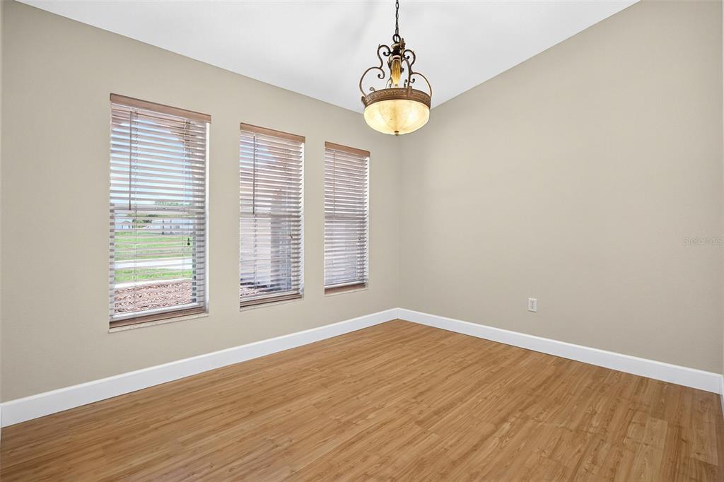An empty dining room features light wood-look flooring, beige walls, and a decorative hanging chandelier — 3318 JERICHO STREET, PORT CHARLOTTE, FL