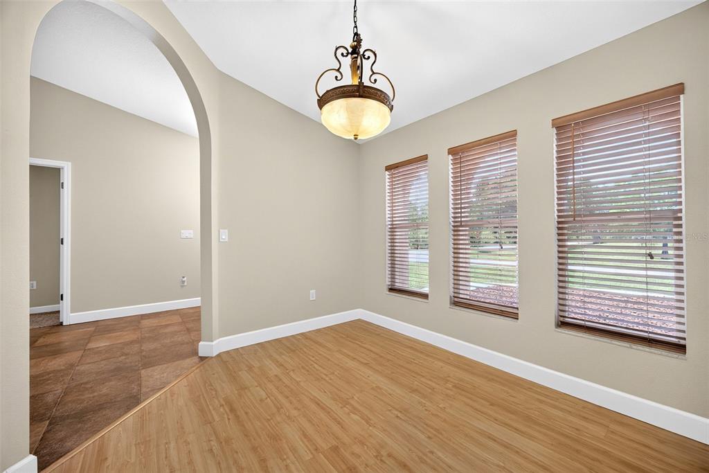 An empty dining room features light wood flooring, three windows with blinds, and a hanging chandelier — 3318 JERICHO STREET, PORT CHARLOTTE, FL