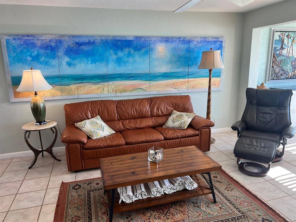 A living room features a brown leather sofa, a coffee table, and a large beach mural — 6006 MIDNIGHT PASS ROAD UNIT 40, SARASOTA, FL