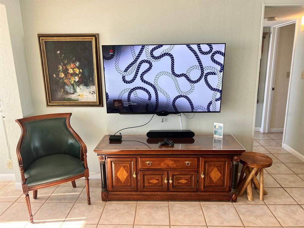 A living room features a wall-mounted television above a wooden media console and green chair — 6006 MIDNIGHT PASS ROAD UNIT 40, SARASOTA, FL