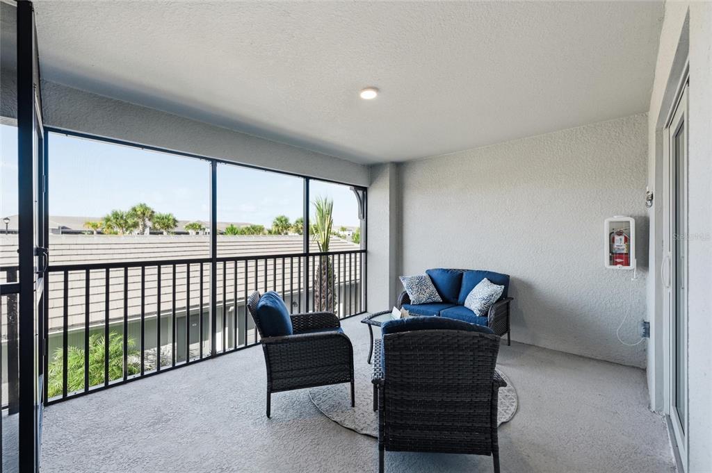 A covered balcony features wicker patio furniture, a screened railing, and a wall-mounted fire extinguisher — 17505 OPAL SAND COURT UNIT 207, VENICE, FL