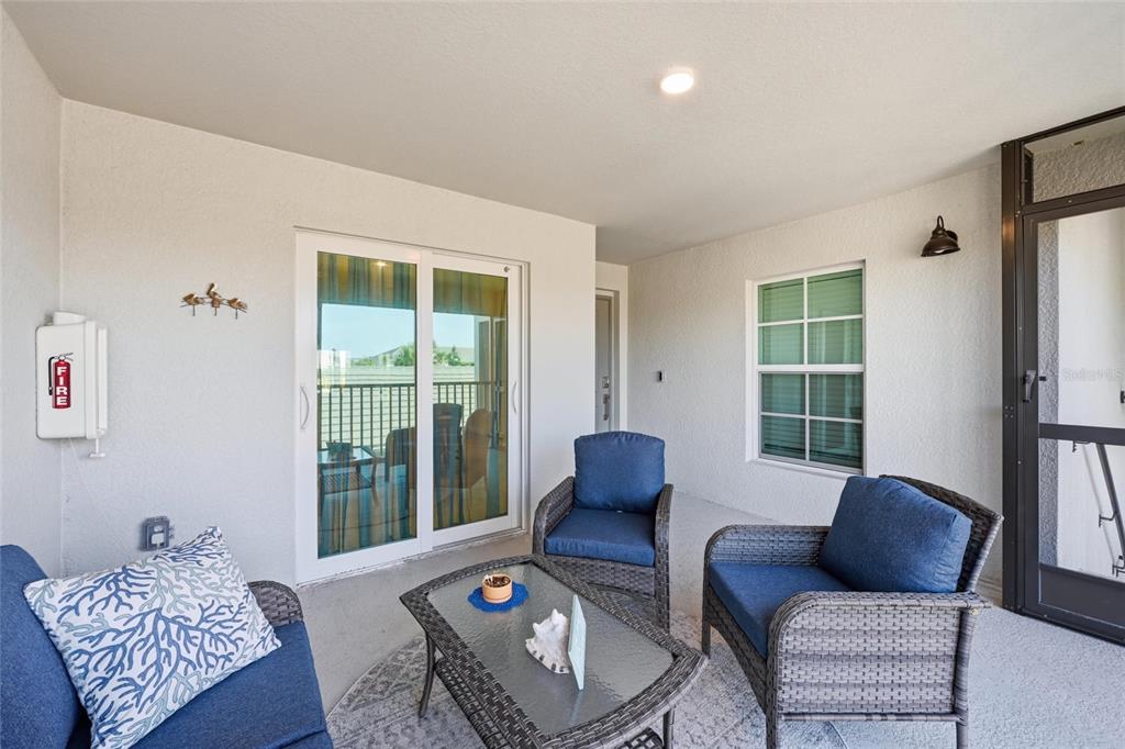 A covered balcony features wicker furniture with blue cushions, a glass-top table, and sliding doors — 17505 OPAL SAND COURT UNIT 207, VENICE, FL