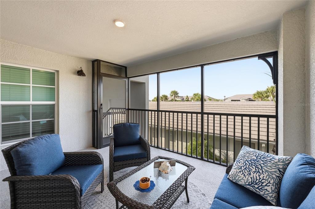 A screened-in balcony features wicker patio furniture and a view of neighboring rooftops — 17505 OPAL SAND COURT UNIT 207, VENICE, FL