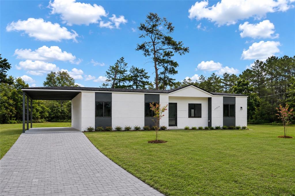 A modern, single-story white house with a black-trimmed carport and dark window accents — 12959 SW 35TH CIRCLE, OCALA, FL