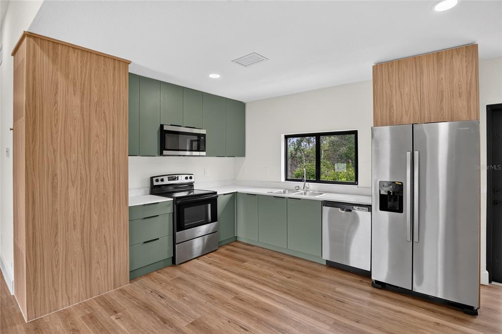 A kitchen features sage green cabinetry, wood-look flooring, stainless steel appliances, and white countertops — 12959 SW 35TH CIRCLE, OCALA, FL