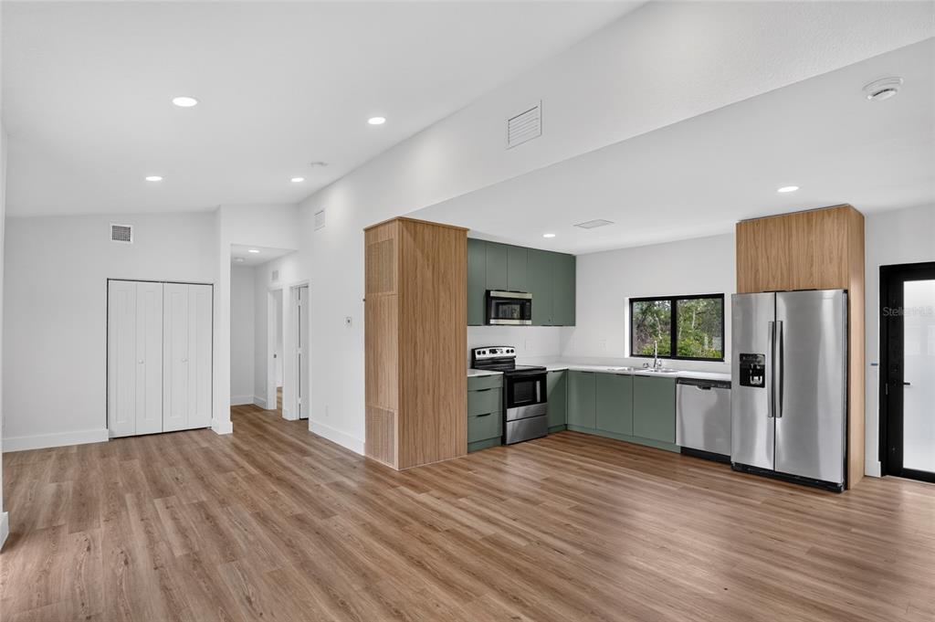 A kitchen with sage green cabinets and wood-paneled accents opens into a spacious living area — 12959 SW 35TH CIRCLE, OCALA, FL